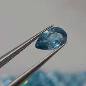 Pear-shaped faceted natural zircon gemstone held with tweezers by a gemologist, showing clarity and sparkle